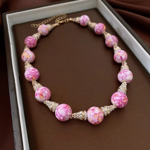Dettaglio di perle di marmo rosa e distanziatori dorati con strass su collana vintage