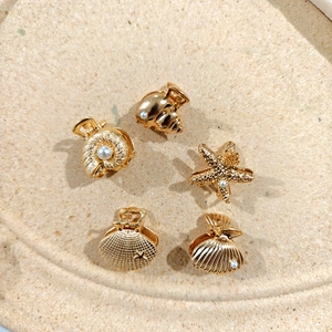 Detailed view of 5 golden mini hair claws with shell shapes and faux pearls
