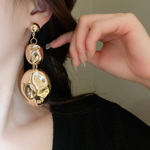 Close-up of model wearing large gold irregular spherical earrings with metallic luster