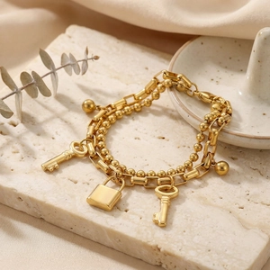 Double-layer gold beaded chain bracelet with key and lock charms on stone surface