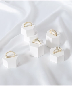 Detail of gold pearl rings on a white hexagonal stand with soft silk background