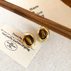 Detail of vintage gold-plated earrings with tiger eye stone on a textured background