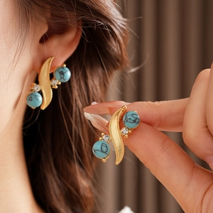 Detail of vintage gold S-shaped earrings featuring turquoise beads and zircon accents