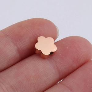Close-up of rose gold flower-shaped stainless steel bead held on a fingertip