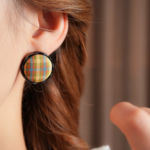Close-up of a round plaid fabric earring with yellow base and black border worn by a model