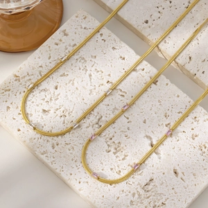 Detail of 18K gold plated snake chains with square zircon pendants on travertine stone