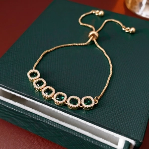 Close-up of adjustable gold bracelet featuring square green gemstones and zircon accents