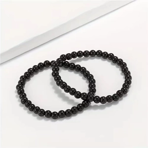Two pieces of 8mm polished black stone beaded bracelets on a white minimalist background