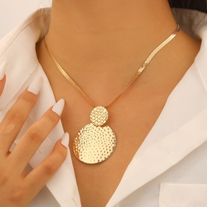Macro detail of golden hammered double circle pendant and flat snake bone chain on model