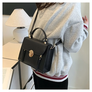 Chic black leather shoulder bag with gold clasp shown in a cozy home setting