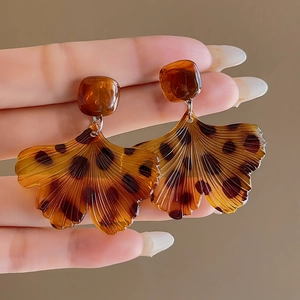 Detail view of resin fan-shaped leopard print earrings held in hand for scale