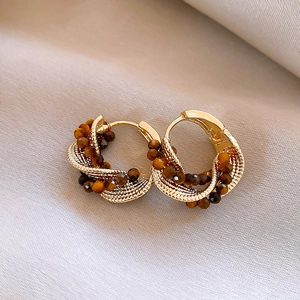 Macro shot of gold-plated tiger eye drop earrings with intricate woven metal texture