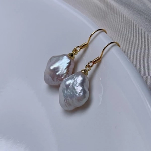Macro view of white baroque pearl clover earrings with gold hooks on silk