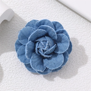 Detailed view of blue denim camellia brooch with vintage frayed edges on white surface