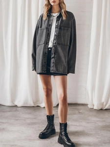 Full body view of a woman in oversized dark grey denim shirt with black mini skirt and tall boots