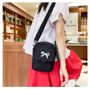 Detail of a black crossbody square bag featuring a stylish white decorative bow
