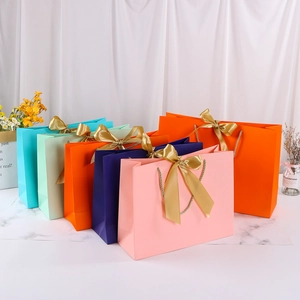 Colorful paper gift bags with golden ribbon handles and bows on a marble table