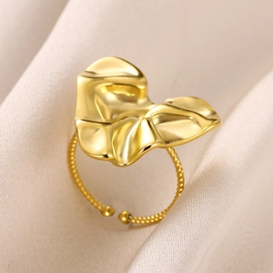 Detailed shot of golden irregular leaf ring with twisted band on soft beige silk background