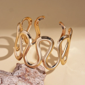 Detailed view of a gold wavy geometric open bangle displayed on a natural rock texture