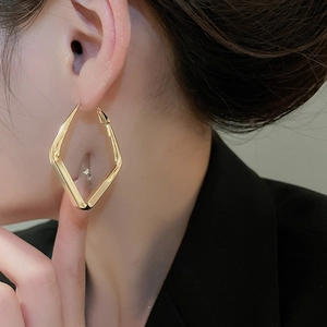 Close-up of geometric diamond-shaped golden metal earrings worn by a model in soft lighting