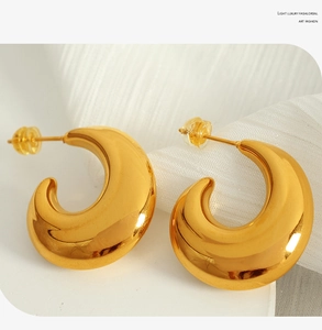 Detailed macro shot of high-polished gold C-shaped hoop earrings on a white display stand