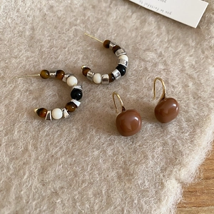 Detailed flat lay of Tiger Eye stones C-shaped square earrings on beige felt background