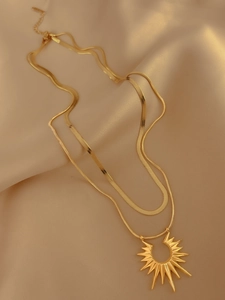 Double-layered gold sunburst pendant necklace with a sleek snake chain on champagne silk