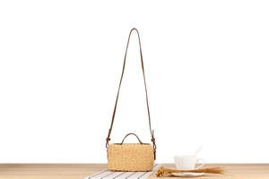 Close-up of beige woven crossbody bag on wooden table with coffee cup and dried flowers