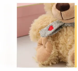 Primer plano de un oso de peluche beige con bufanda gris de punto y un corazón rojo bordado