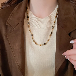 Détail du collier de perles œil de tigre vintage sur daim marron et maille beige