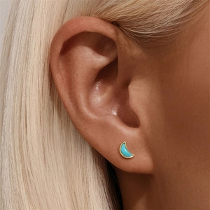 Close-up of golden crescent moon stud earrings with turquoise inlay worn by a model
