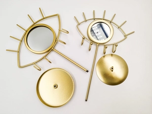 Flat lay view of golden eye-shaped jewelry display stand parts with round base and mirror