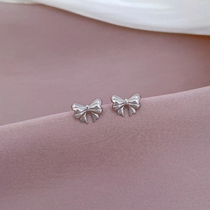 Macro shot of silver bow stud earrings on purple silk featuring mirror polished titanium steel