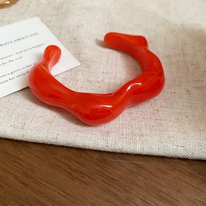 Macro detail of glossy bright orange wavy acrylic resin bangle on rustic linen texture