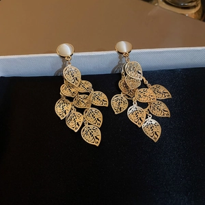 Close-up of golden hollow leaf tassel earrings with white opal stone on black velvet