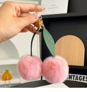 Macro shot of pink rabbit fur cherry keychain with leather leaf and gold metal clasp