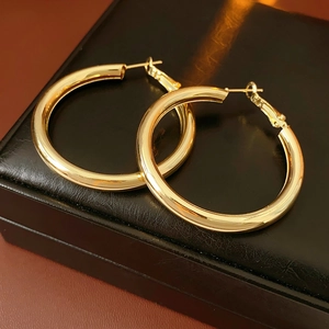 Close-up of golden metallic hoop earrings on black leather surface with warm light