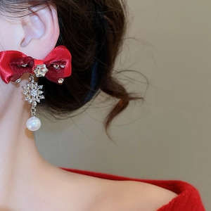 Detailed close-up of a red fabric bow earring with a silver snowflake and pearl drop