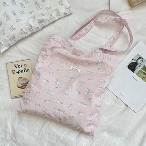 Detail of pink canvas tote with blue cat print and brand tag on a cozy bed background