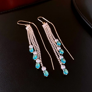 Detail view of gold tassel earrings featuring water-drop blue crystals on dark leather
