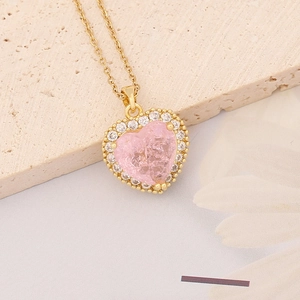 Macro detail of gold necklace with pink heart pendant surrounded by clear crystals