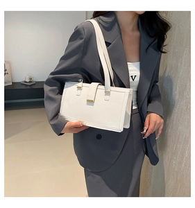Detailed view of a white leather tote bag with gold buckle on a model in a grey suit