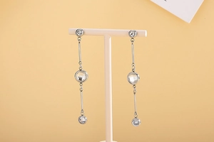 Close-up of silver tassel earrings with three round zircons on a white display stand