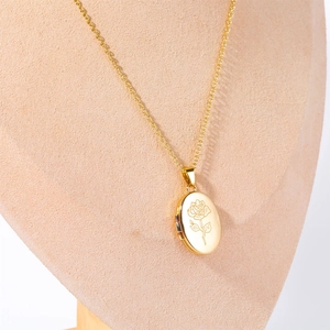 Close-up of golden oval locket necklace with rose engraving on a beige velvet mannequin