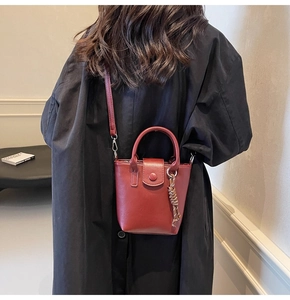 Detailed side view of a burgundy bucket bag with top handle and woven tassel charm