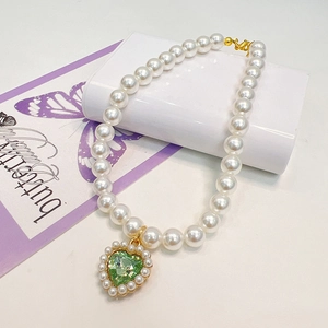 Detail of a pearl cat collar with a heart-shaped green crystal pendant and gold clasp
