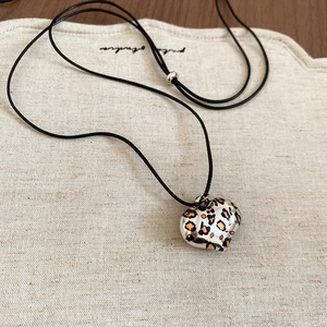 Leopard print heart pendant necklace with adjustable black wax cord on a textured mat