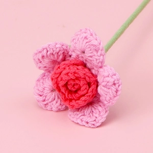 Macro detail of hand-crocheted yarn rose with pink and red petals on a solid pink backdrop
