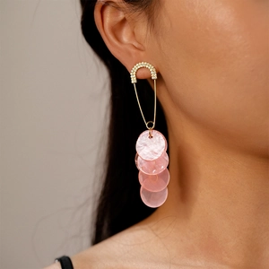 Close-up of dangling safety pin earrings with rhinestones and pink shell-like disks