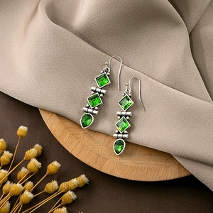 Detailed close-up of retro silver drop earrings with green crystals on a wooden stand